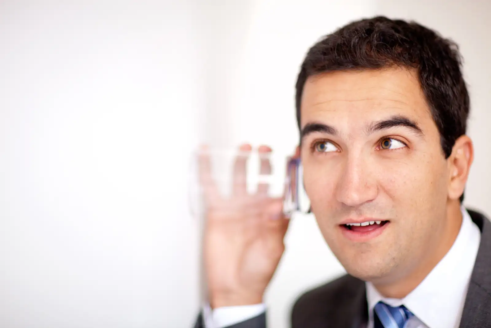 Business man spying with a glass through a wall.jpeg