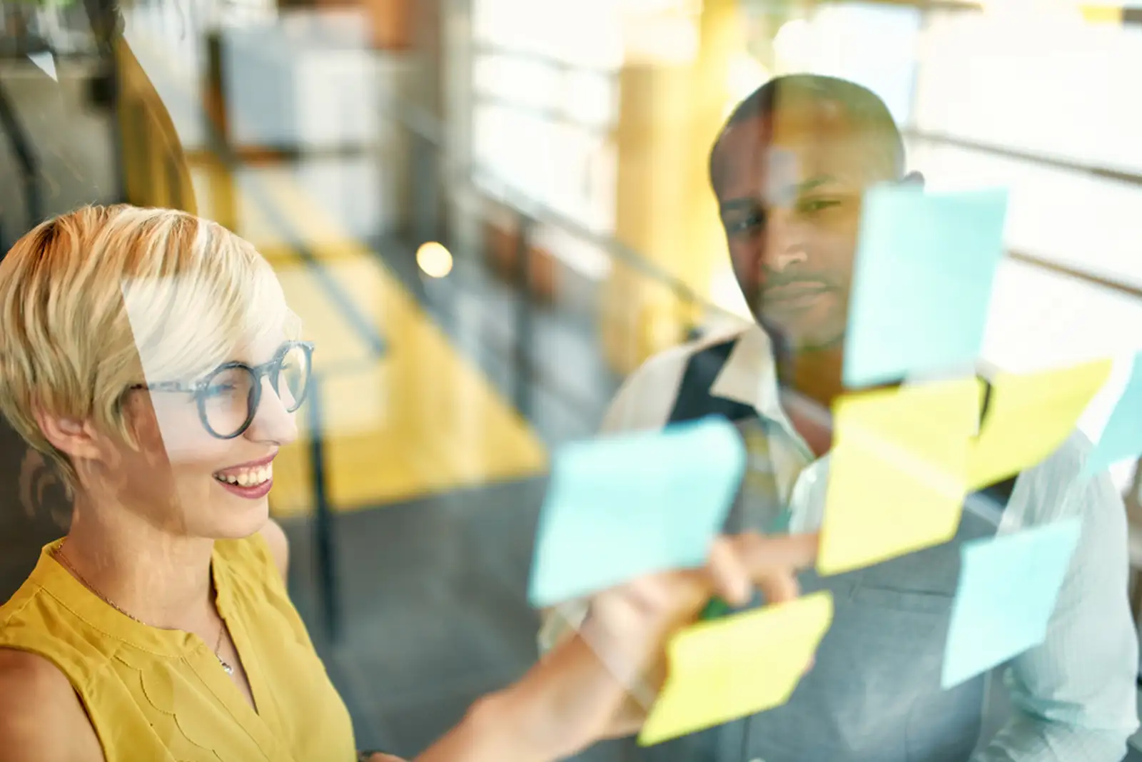 Two creative millenial small business owners working on social media strategy brainstorming using adhesive notes in windows.jpeg