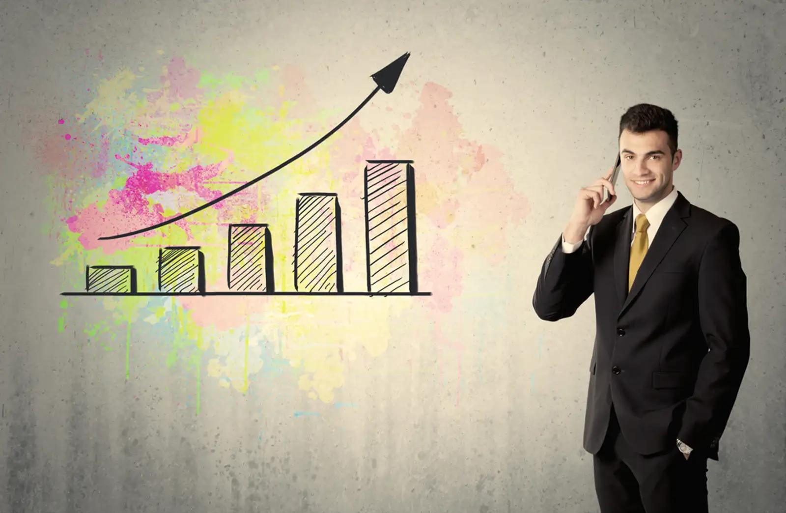 An elegant businessman standing in front of a grey wall with colorful growing chart drawing concept.jpeg