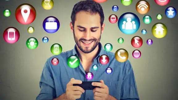 communication technology mobile phone high tech concept. Happy man using texting on smartphone social media application icons flying out of cellphone isolated grey wall background. 4g data plan-1.jpeg