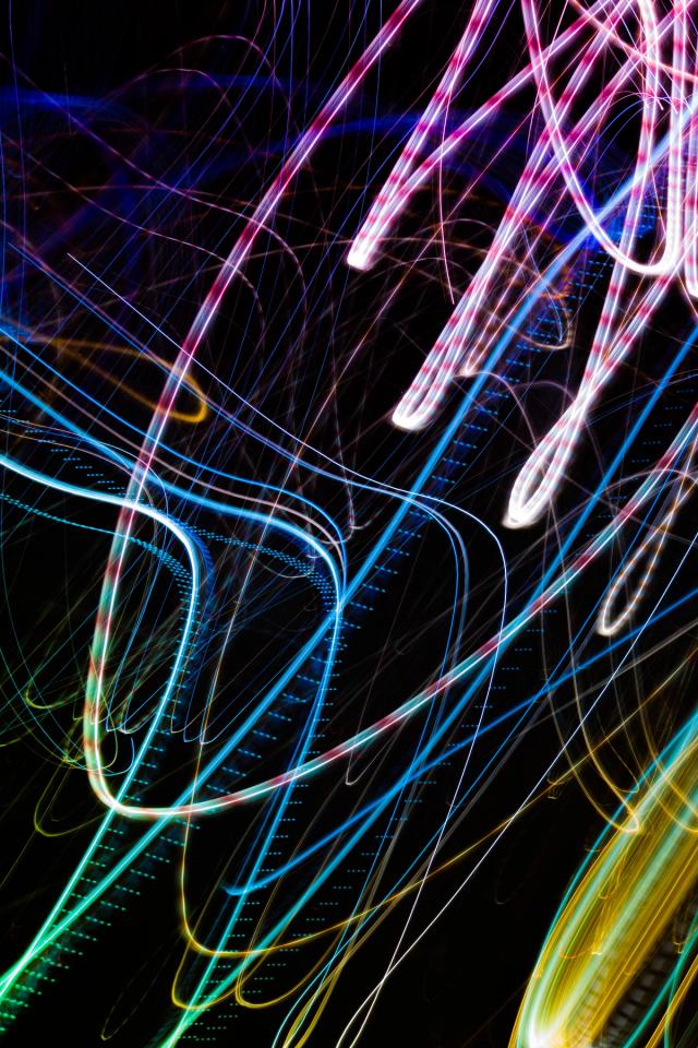 Long-exposure light trails in pink, blue, green and yellow looping across a black frame, like a fairground ride drawn in neon.