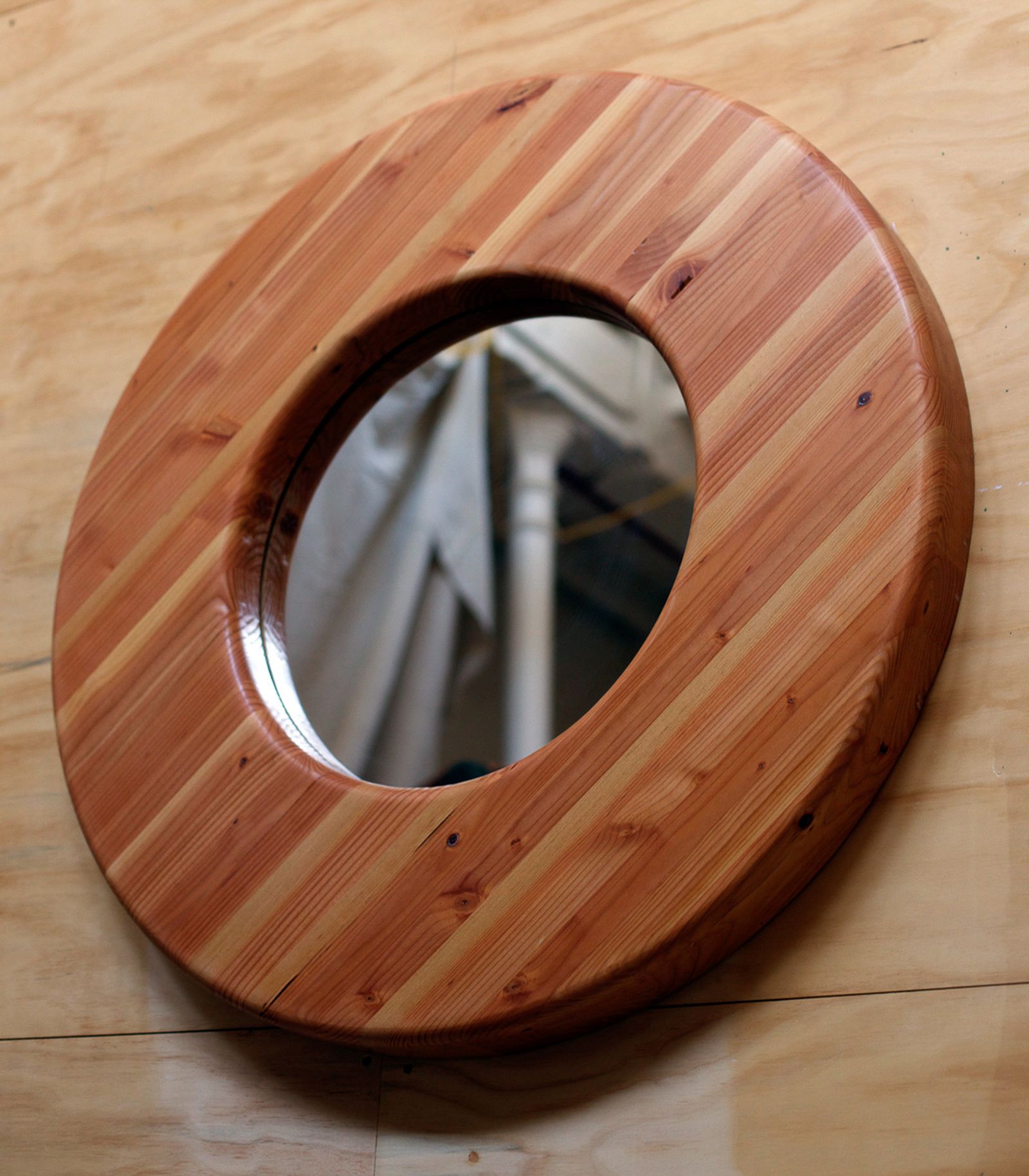 A large round wall mirror with a thick laminated cedar frame, finished with a smooth routed inner edge.