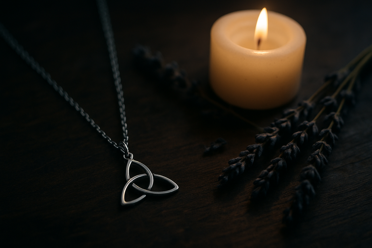 Silver triquetra pendant necklace beside a candle and dried lavender in soft moody light
