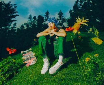 A woman with a skateboard sitting in a grassy field