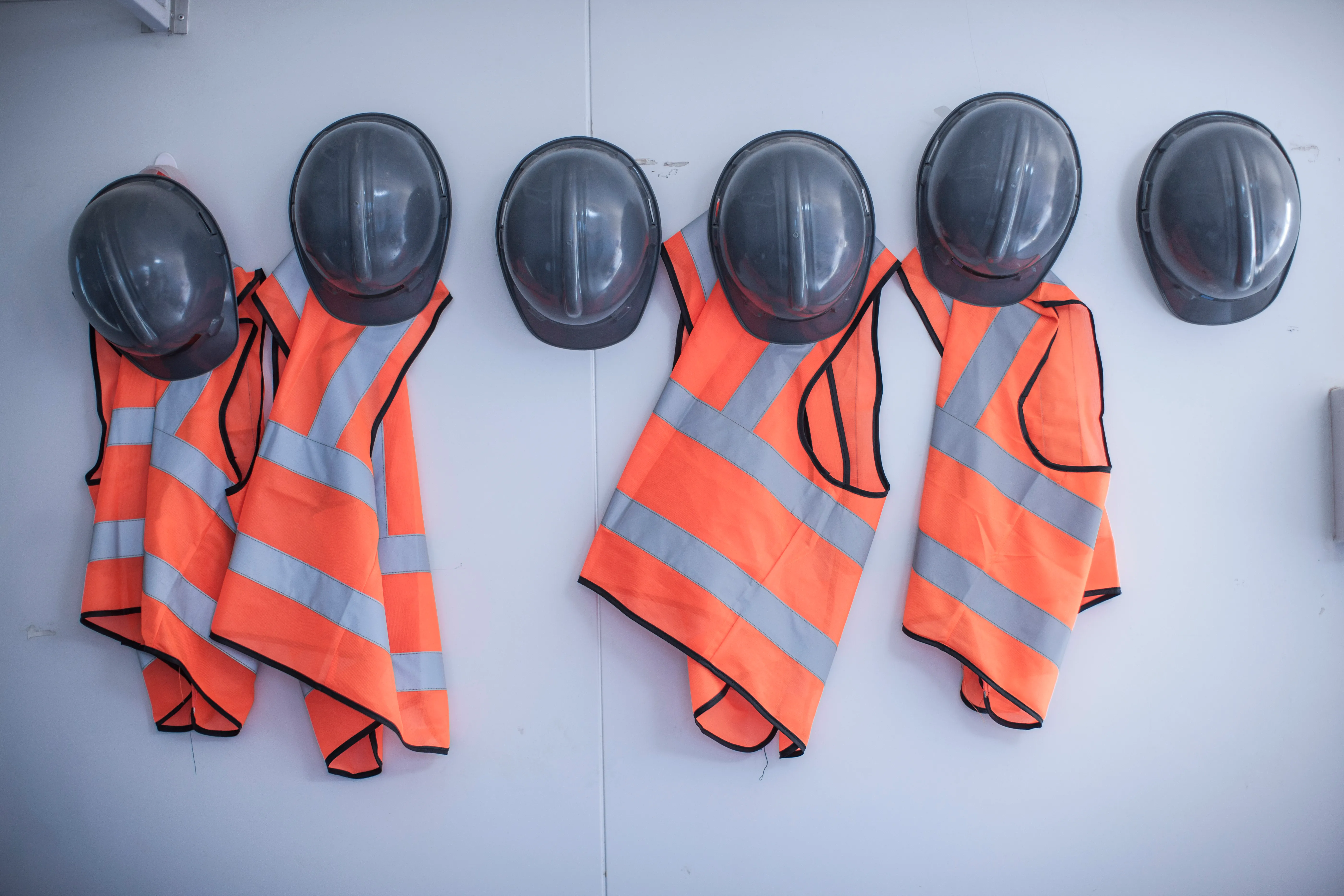 high vis vests and hard hats hanging on a white wall