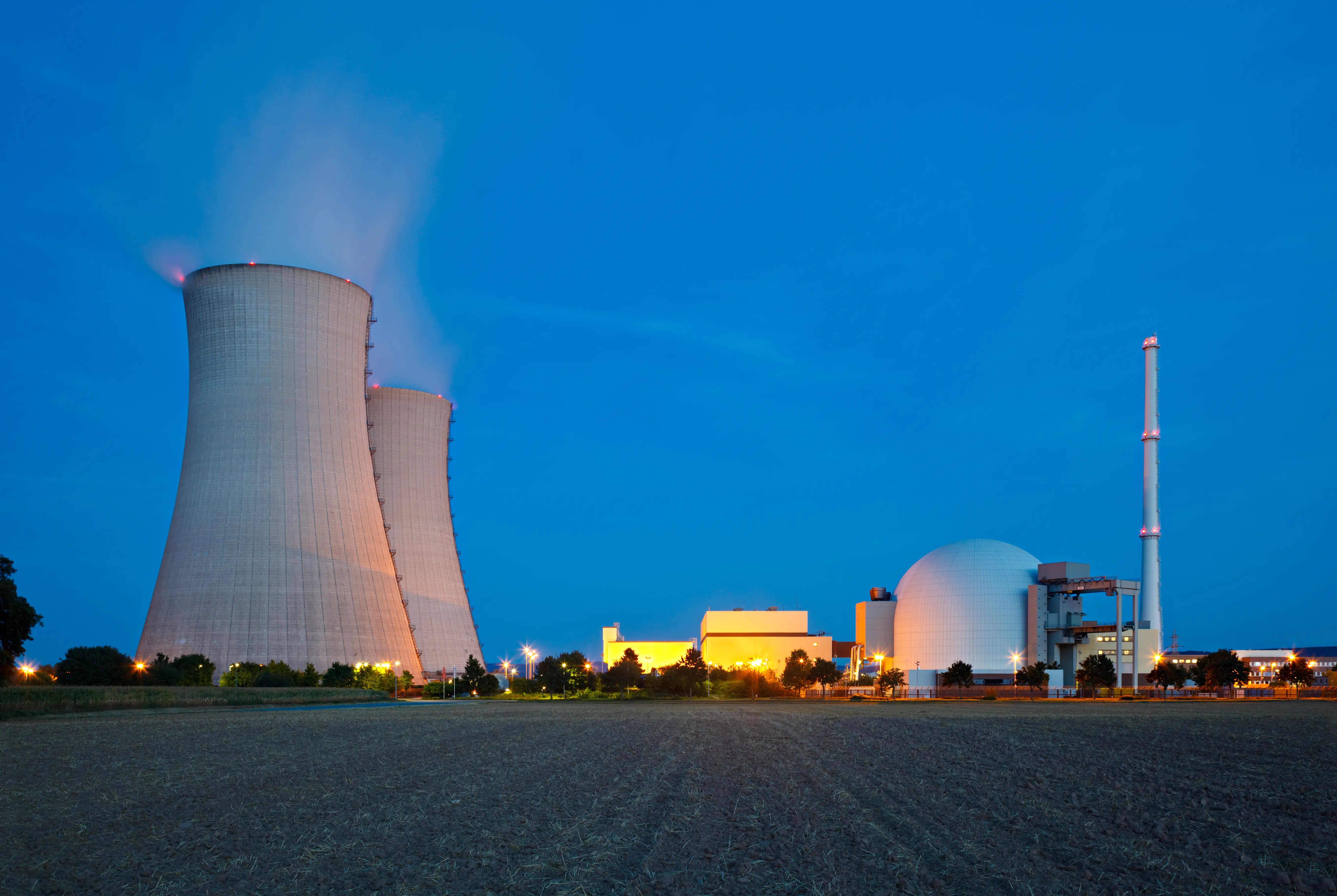 A nuclear power plant with night blue sky, a field as foreground.