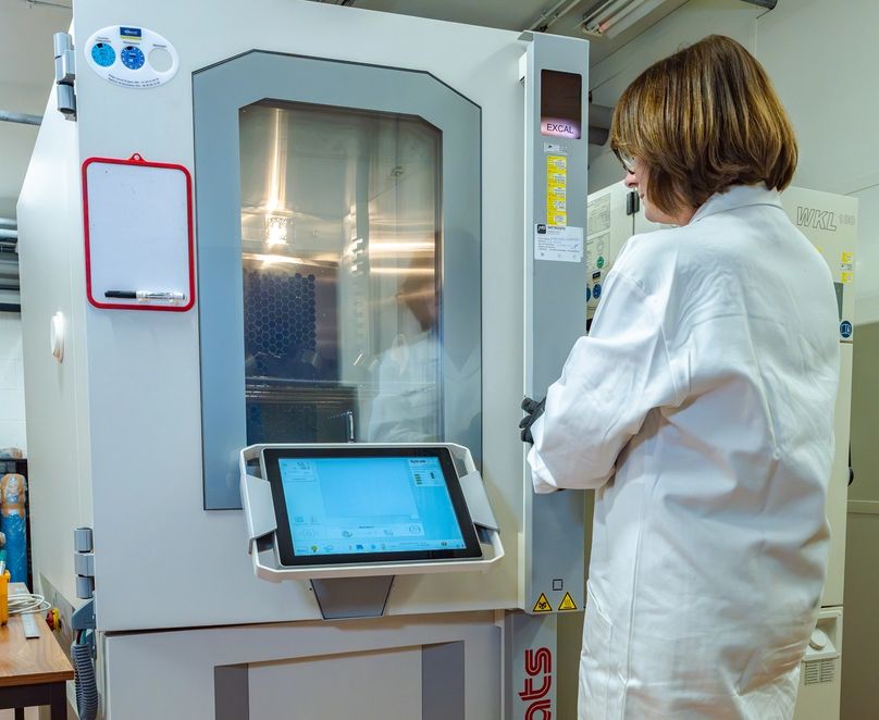 Collaboratrice devant une chambre climatique fermée, regardant le test se dérouler à travers une vitre