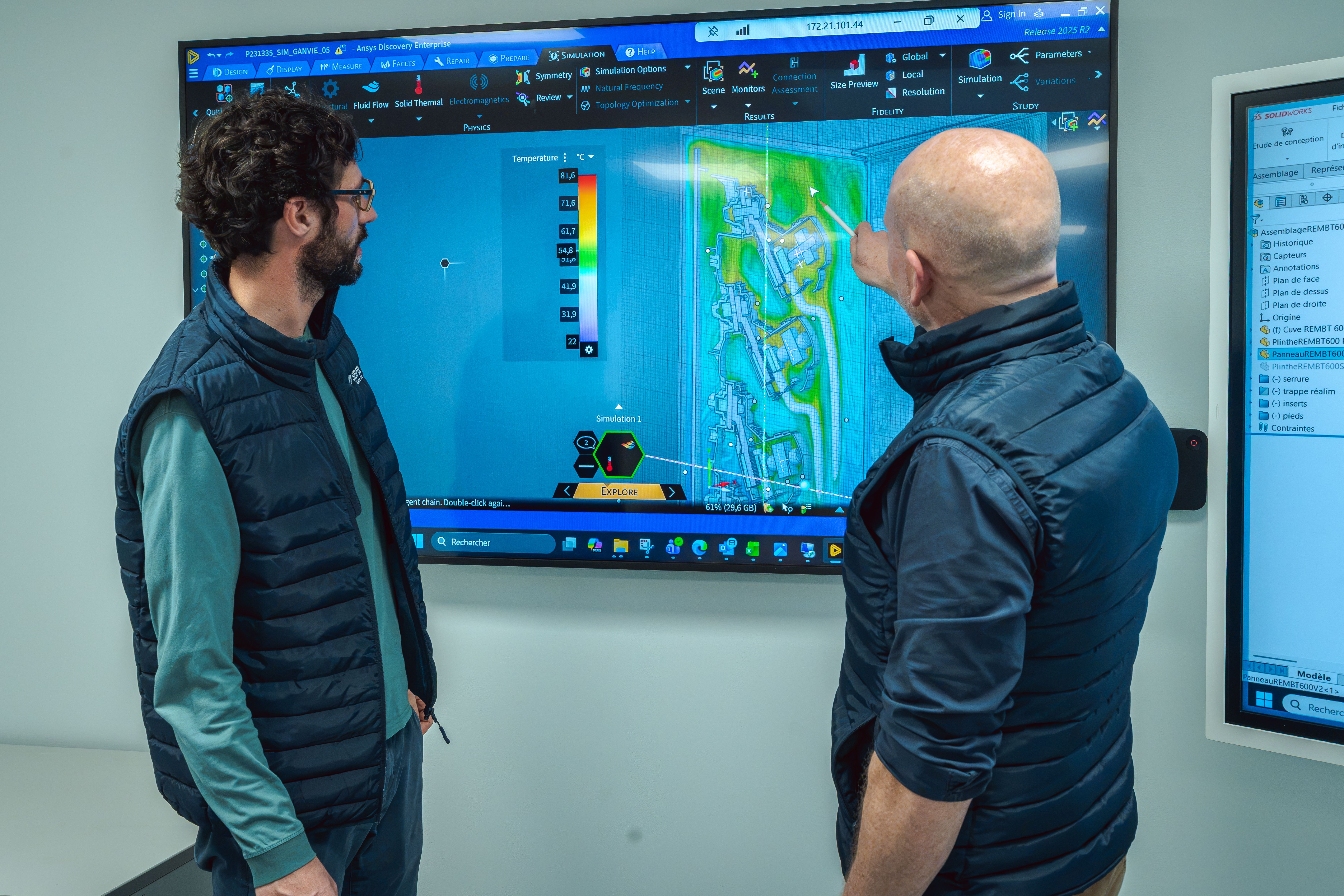 Deux hommes devant une télé affichant une simulation numérique d’une pièce