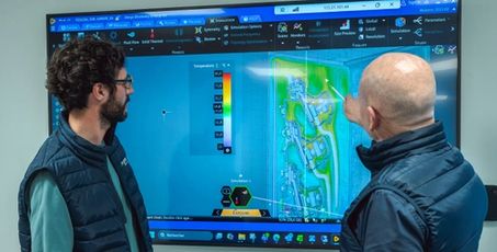 Deux hommes devant une télé affichant une simulation numérique d’une pièce