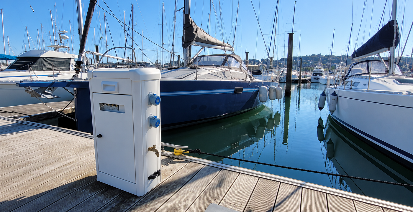Borne connectée sur la jetée d'un port en bord de mer où sont amarrés des bateaux