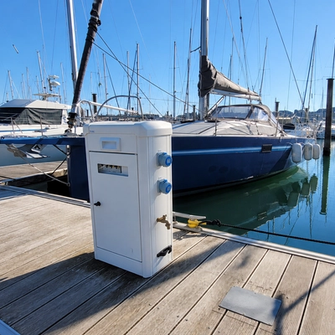 Borne connectée sur la jetée d'un port en bord de mer où sont amarrés des bateaux