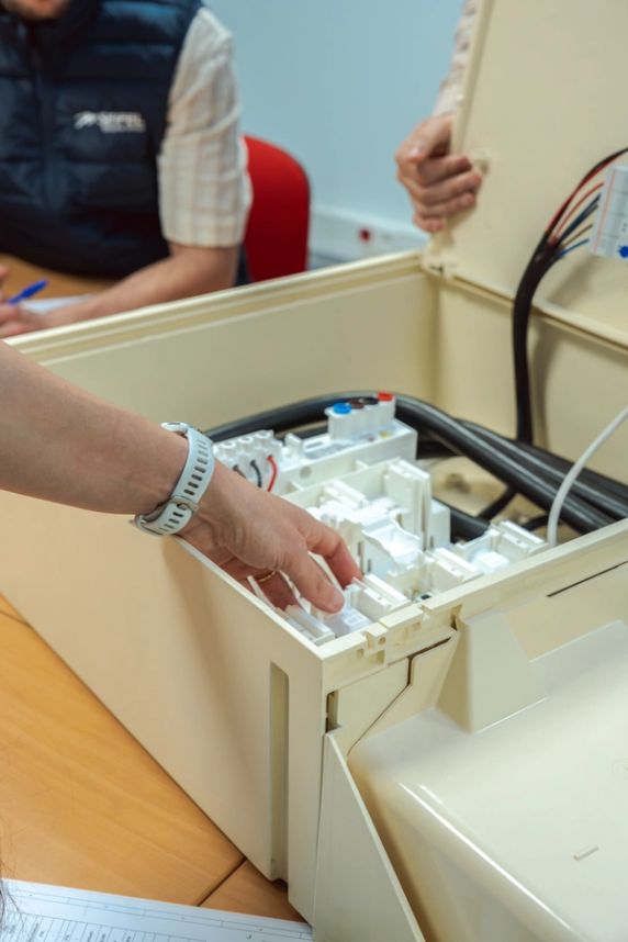 Main montrant une partie à l’intérieur d’un coffret électrique posé sur une table de réunion