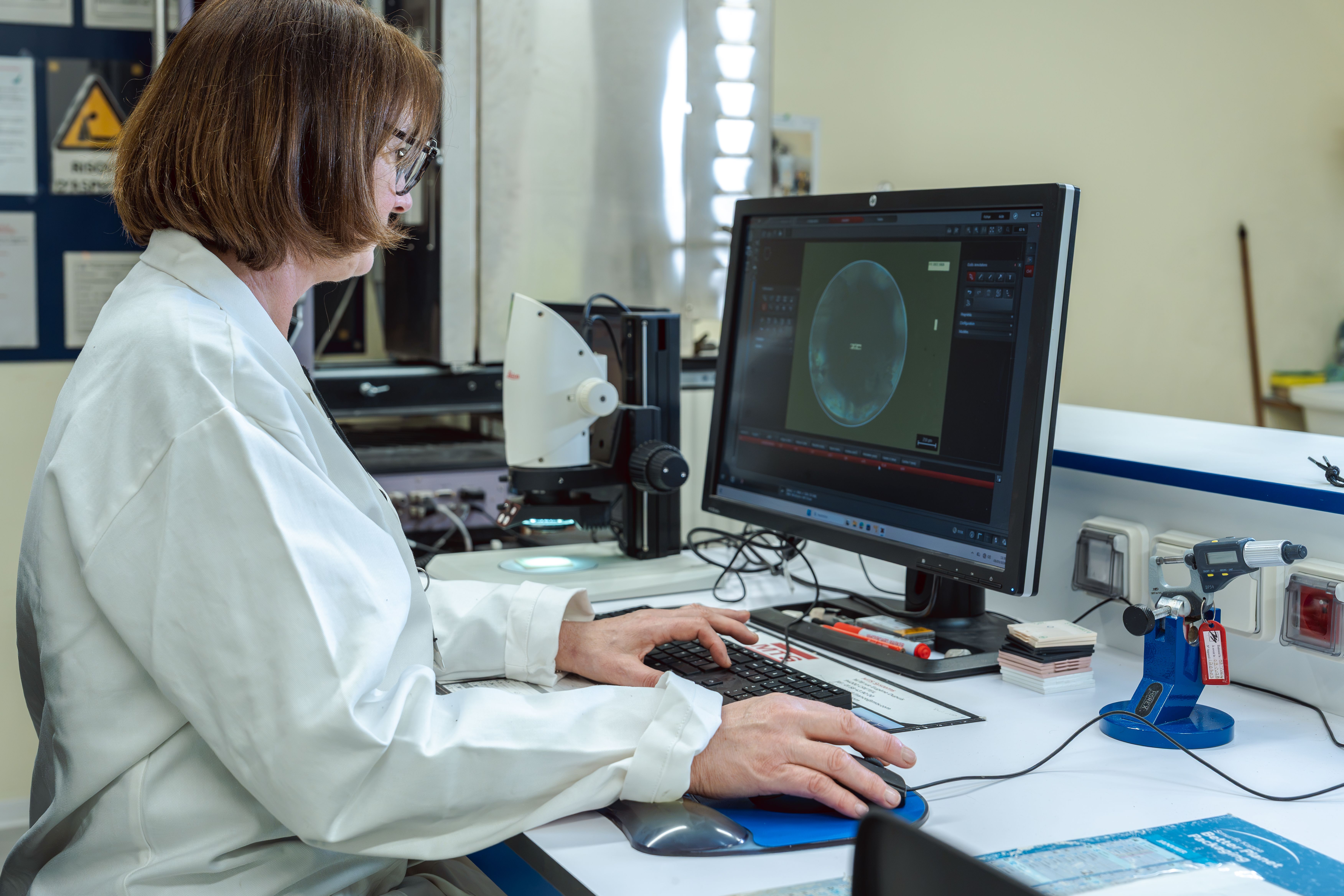 Technicienne assise devant un ordinateur du laboratoire avec des tests à l’écran