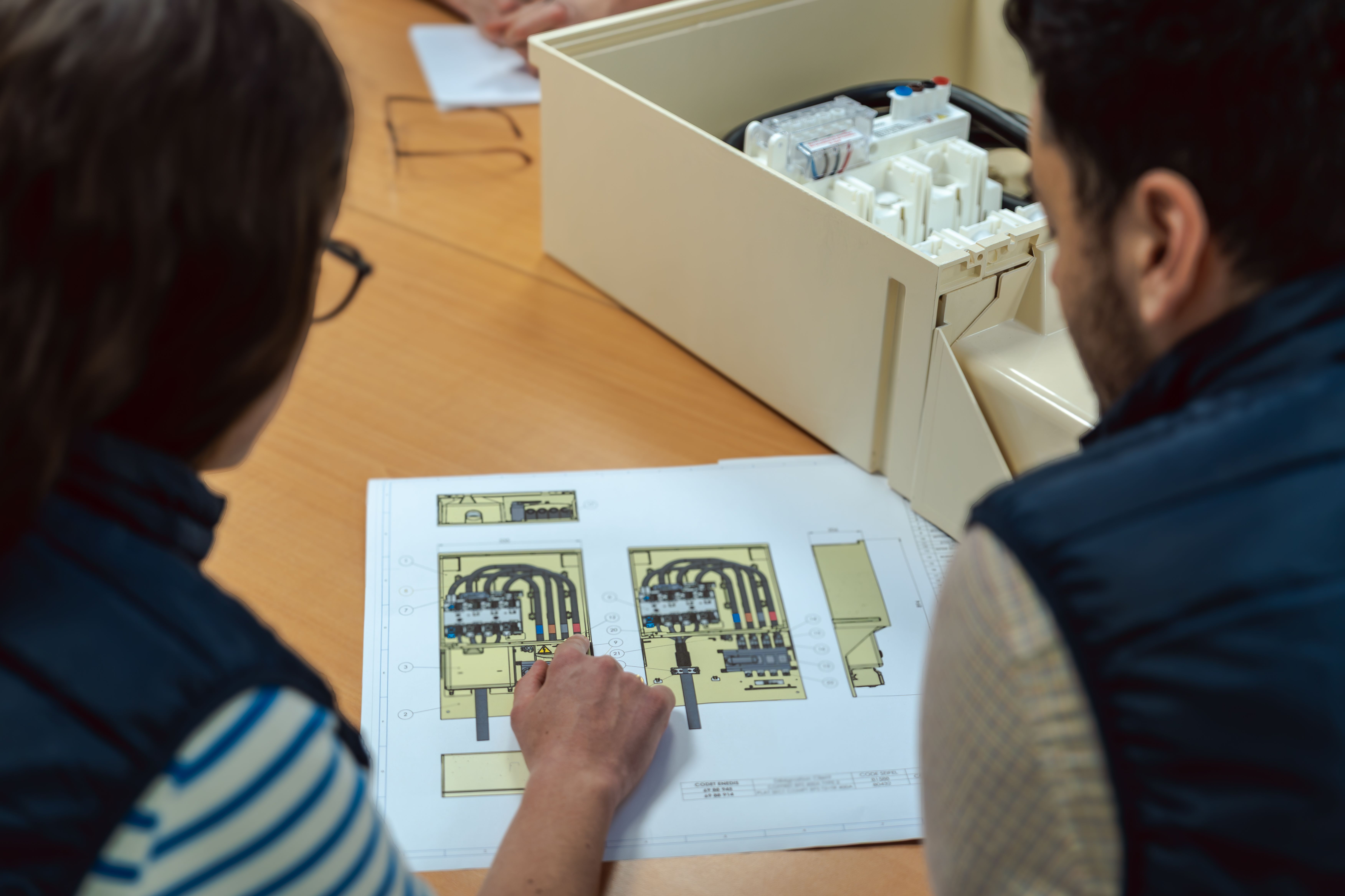 Deux personnes penchées sur une feuille avec un schéma d’un coffret électrique