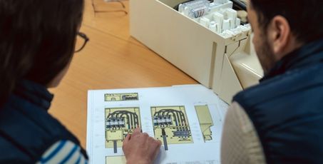 Deux personnes penchées sur une feuille avec un schéma d’un coffret électrique