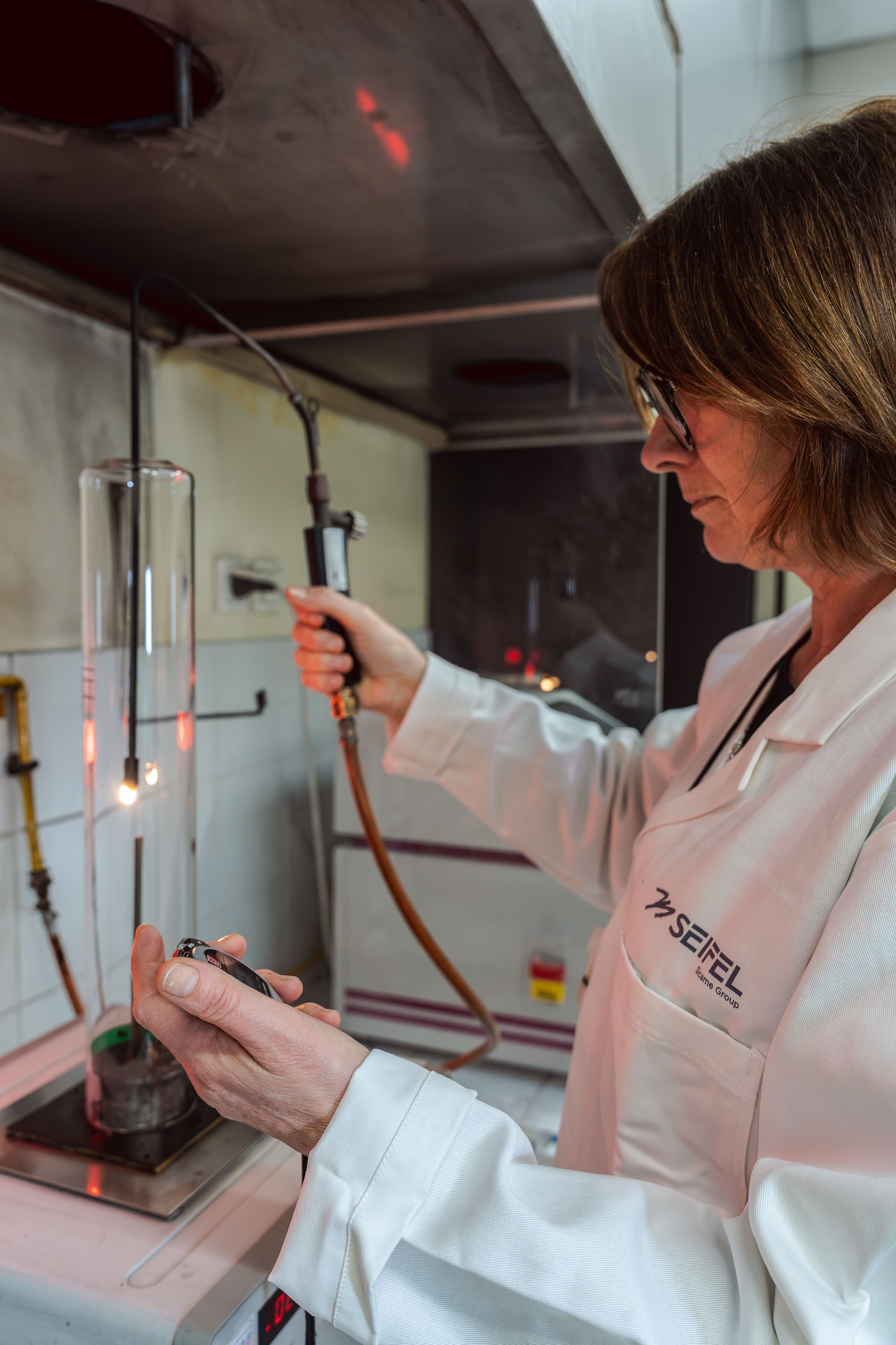 Technicienne en plein test au sein du laboratoire matière avec un chronomètre dans une main et un chalumeau dans l’autre