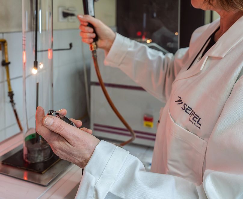 Technicienne en plein test au sein du laboratoire matière avec un chronomètre dans une main et un chalumeau dans l’autre