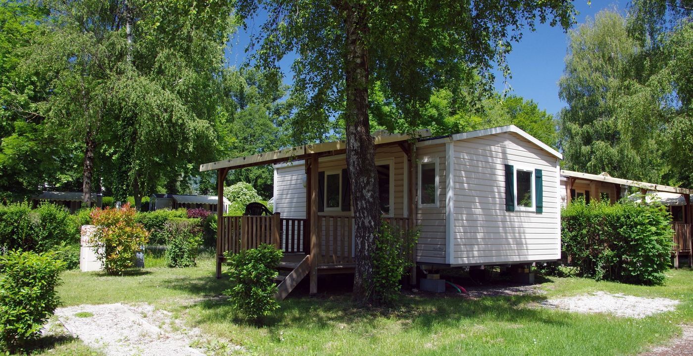 Mobil-home sur un terrain en herbe entouré d'arbres et avec un coffret électrique à côté