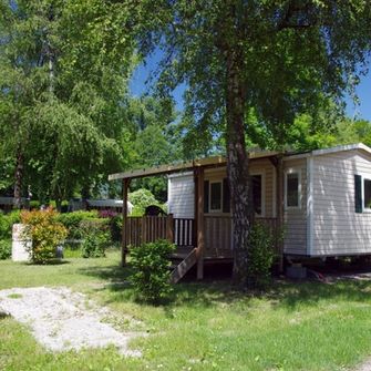 Mobil-home sur un terrain en herbe entouré d'arbres et avec un coffret électrique à côté
