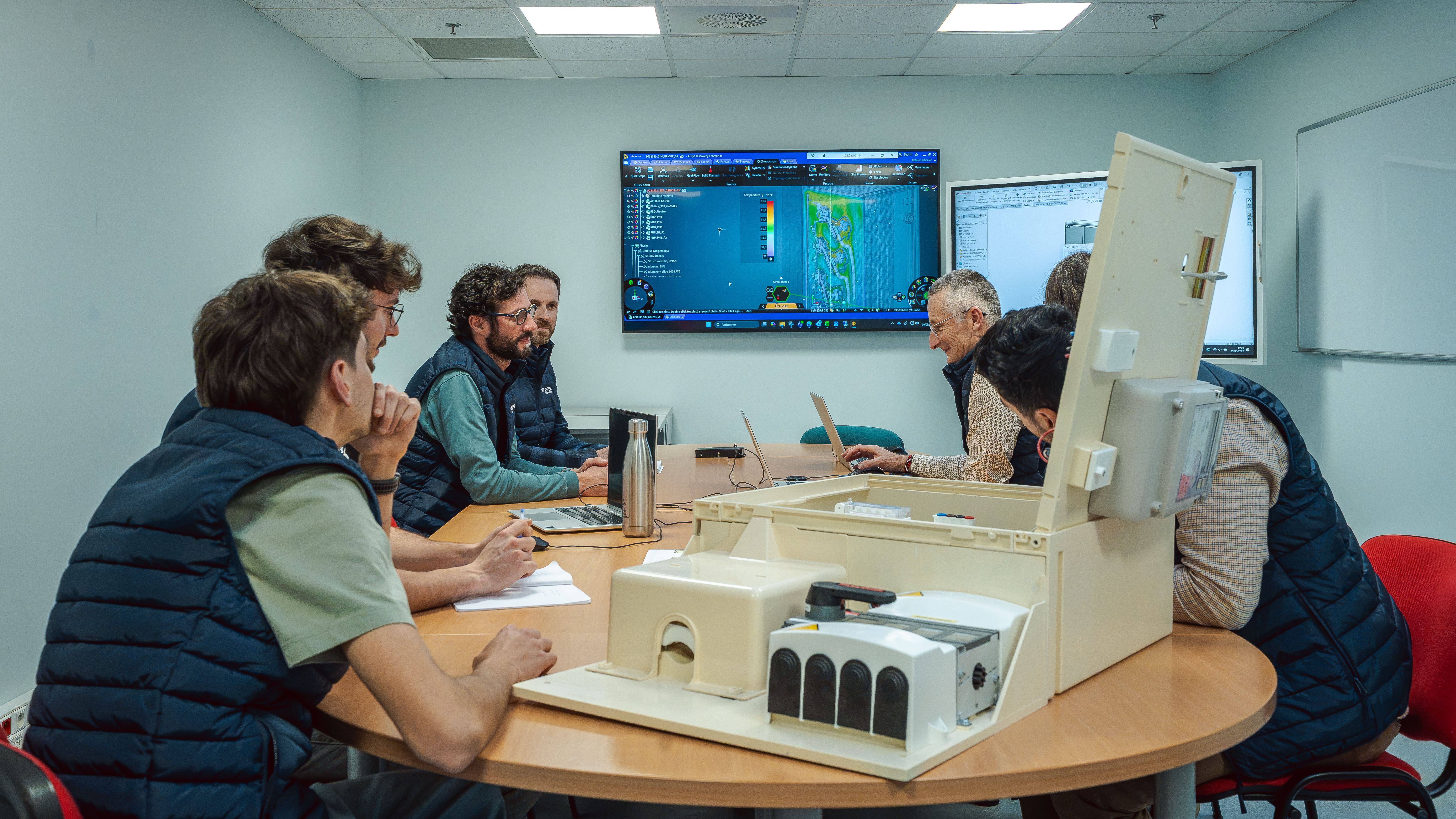 Equipes R&D réunies dans une salle autour d’une table avec un coffret électrique ouvert