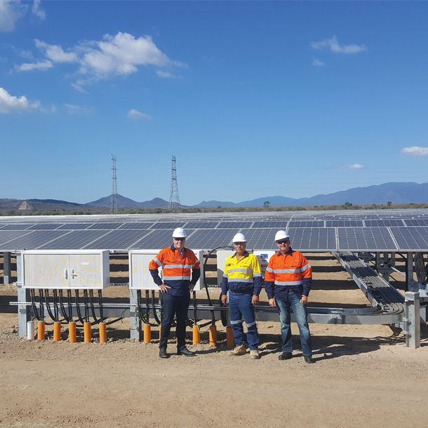 Trois hommes debout en tenue de chantier devant une ferme solaire en Australie
