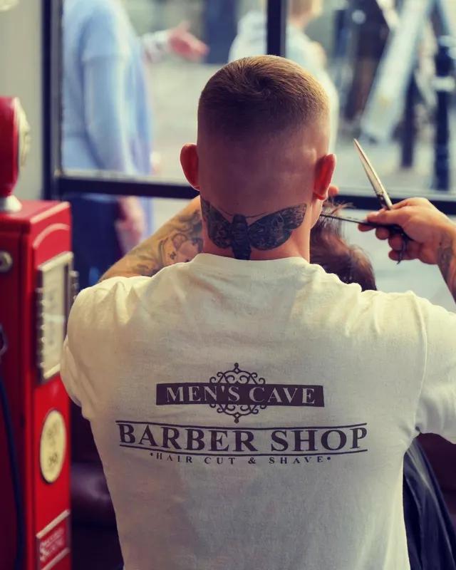 A barber finishing a fade, client's neck tattoo visible