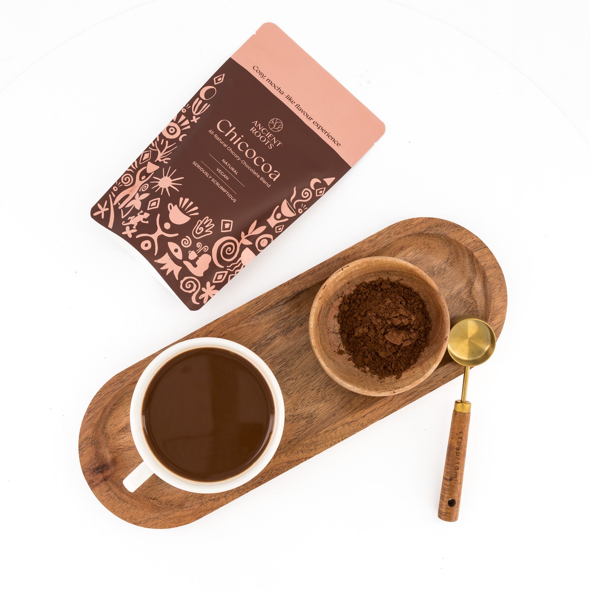 A bag of Ancient Roots Chicocoa lying beside a freshly brewed cup on a tray.