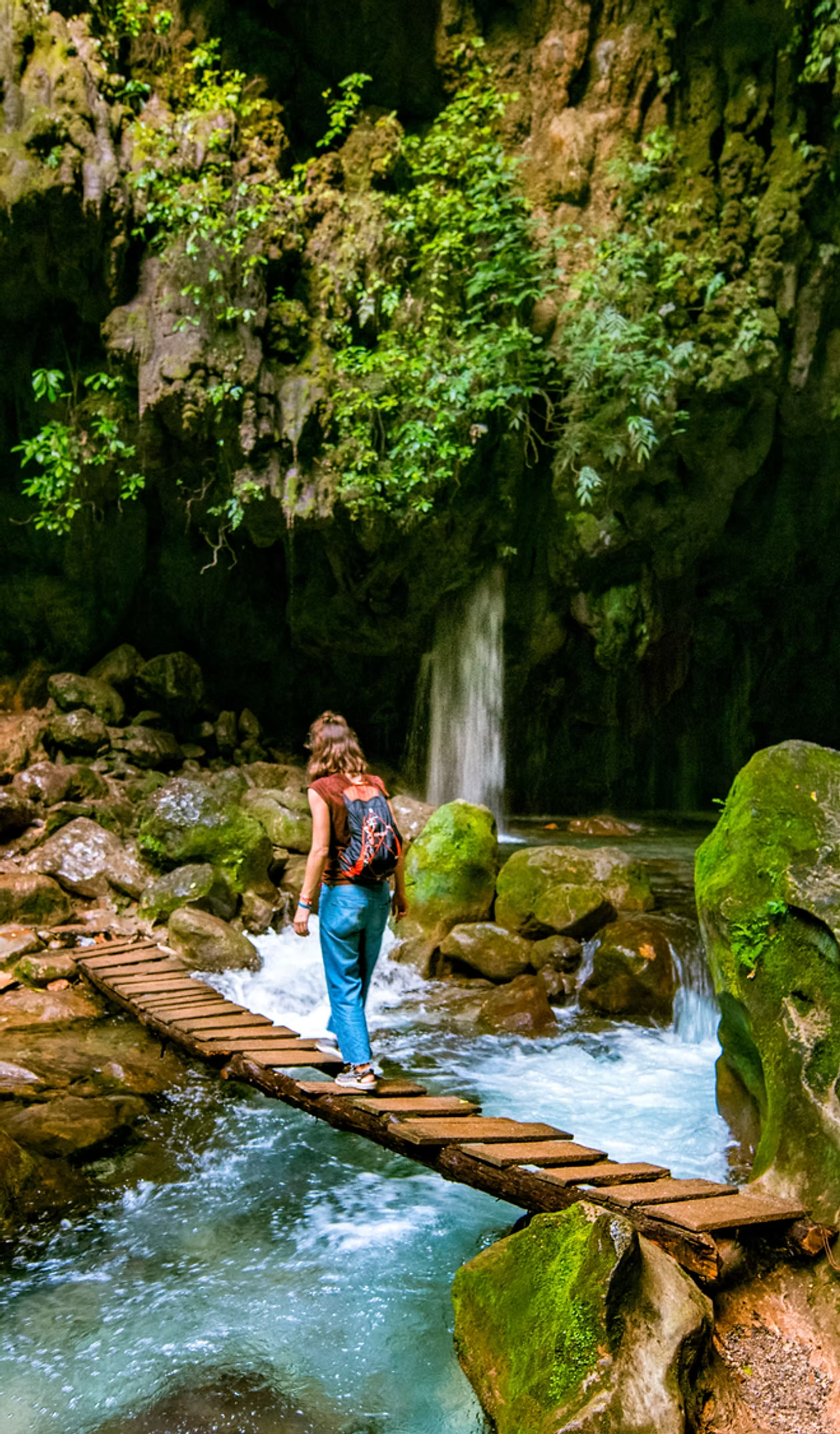 A young woman crossing a bridge over a stream in a lush forest
