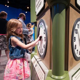 A little girl adjusting the hands of a large clock