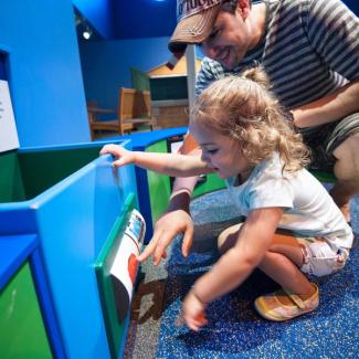 Little toddler girl and father playing with items on an activity wall