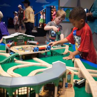 Two little boys playing with trains on large play table with wooden tracks