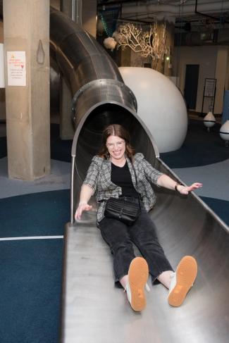 An adult emerges from a metal slide, smiling.