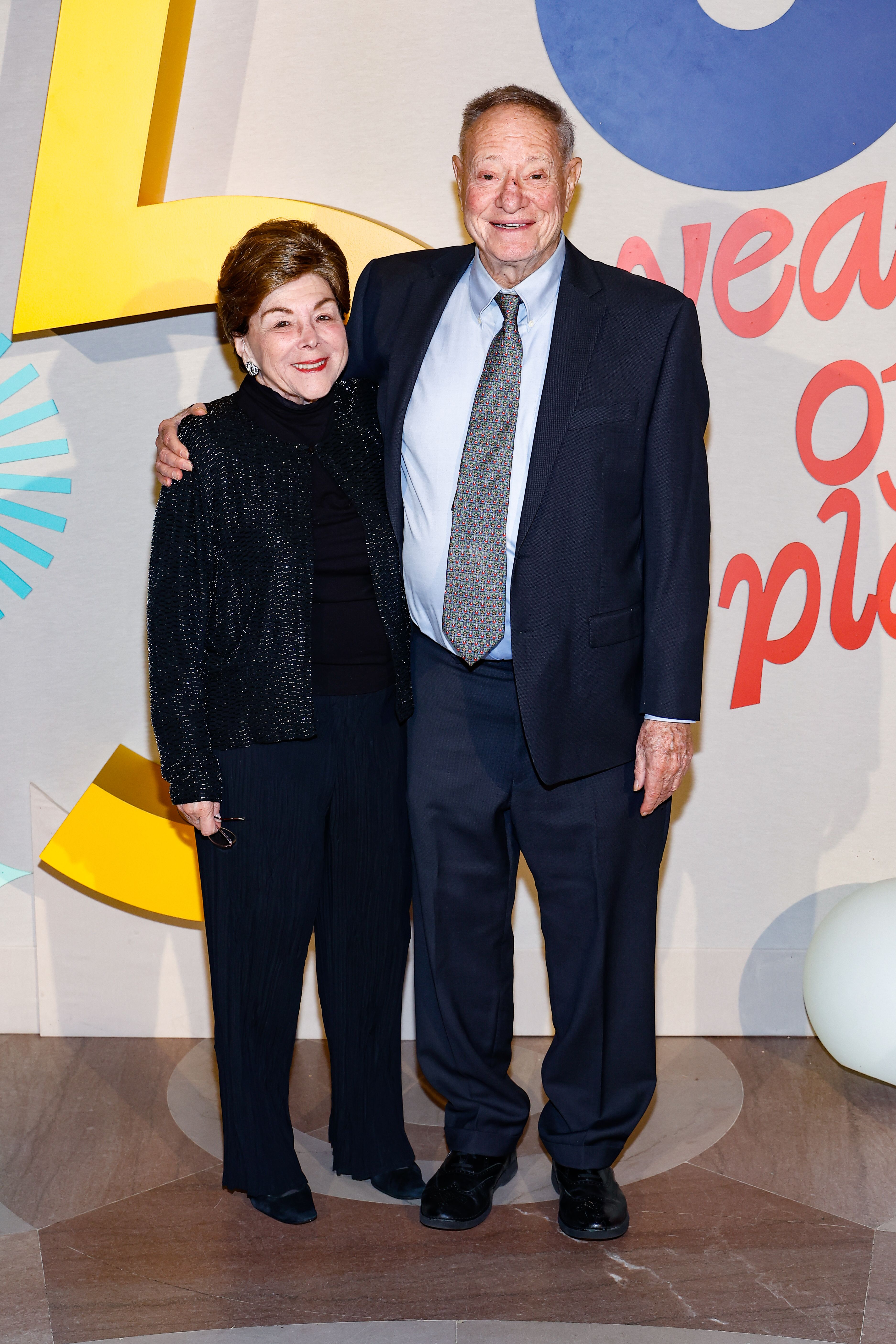 Two people posing in front of the National Children's Museum Dreamers Gala step and repeat. 
