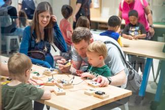 Woman smiles as man shows young child how to connect wires together.