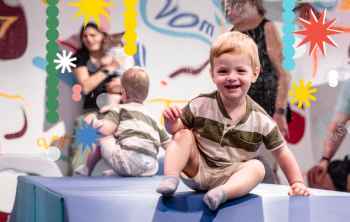 A child sitting in Little Movers exhibit with holiday graphics surrounding him