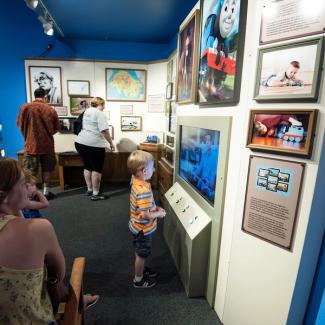 little boy looking at a video on a wall with old historical pictures of thomas the train