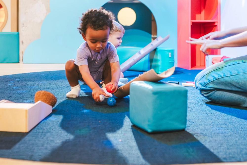 Little boy holding a ball up to a wooden ramp