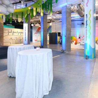 Two bar tables with white cloths stand in a colorful foyer with columns labelled "art + tech" and "climate action heroes."