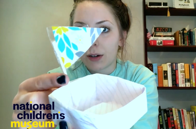 A woman is holding a paper boat up to the camera
