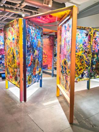 Life-size art installation with colorful painted plastic walls and wooden structure.