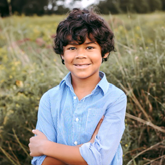 Child Investigator Jack wearing a blue button-up shirt and standing in a grassy field