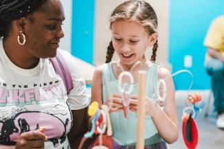 A caregiver and girl smiling in the tinkering corner