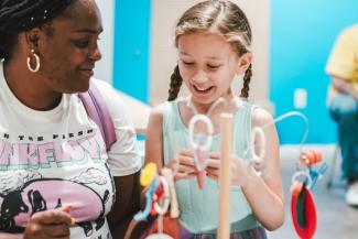 A caregiver and girl smiling in the tinkering corner