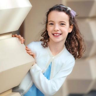 Child Investigator Olivia wearing a white sweater over a blue shirt and peeking out around a corner