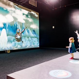 A woman and toddler watch their digital projection against an icy digital background.