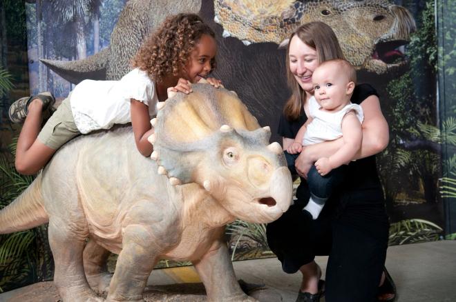 little girl sits atop miniature triceratops, woman holds smiling baby