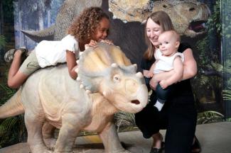 little girl sits atop miniature triceratops, woman holds smiling baby