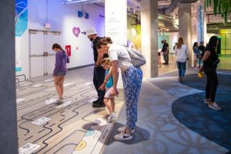 A woman points at a maze decal on the ground as a young girl looks on.