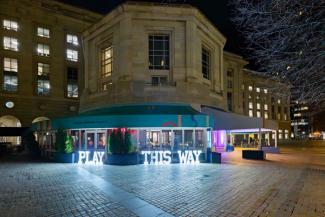 Exterior of the Museum with light signs reading: Play This Way