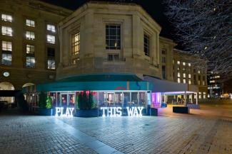 Exterior of the Museum with light signs reading: Play This Way